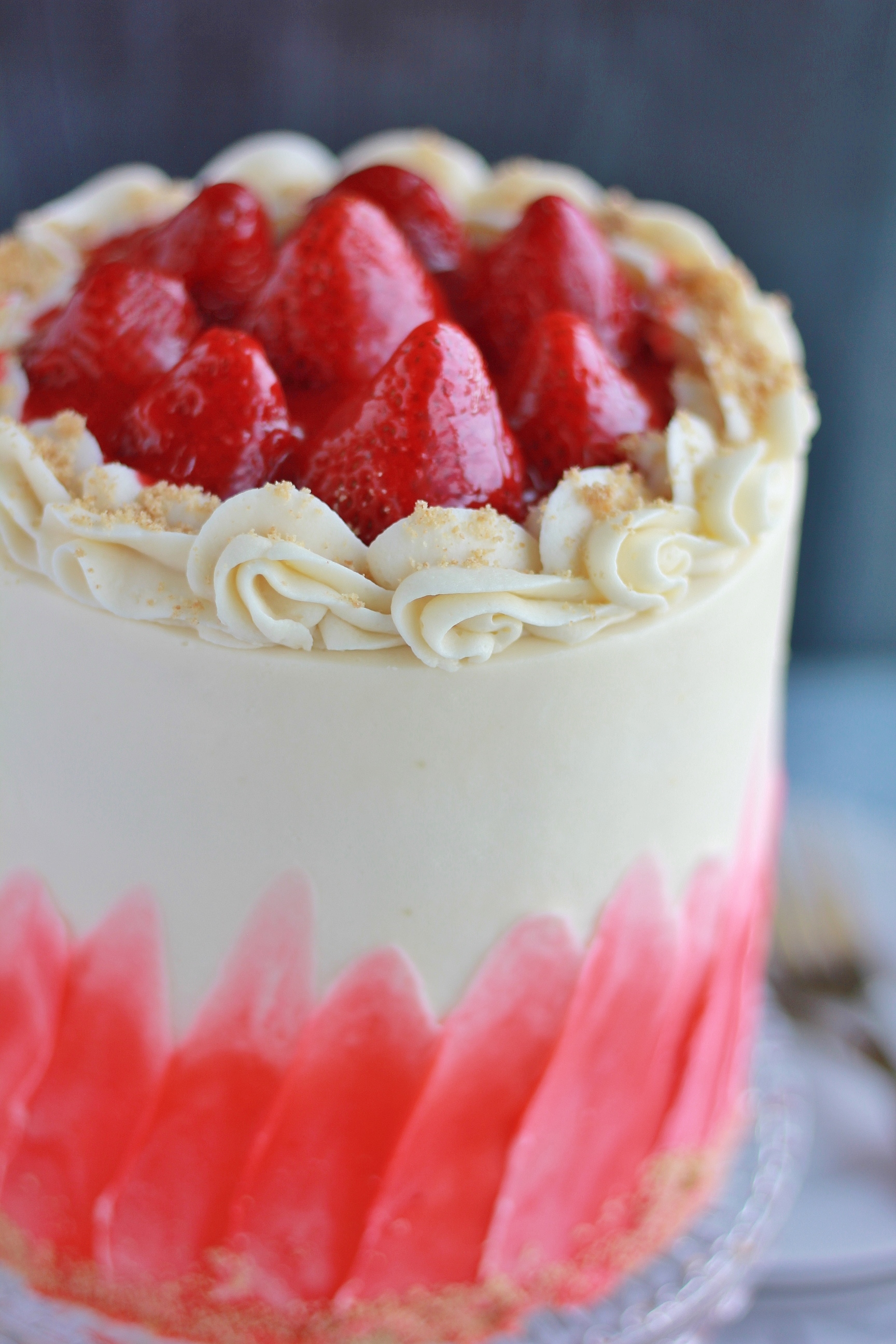 A slice of strawberry cheesecake cake on a white plate, with layers of vanilla cake, strawberry cheesecake, and strawberry frosting.